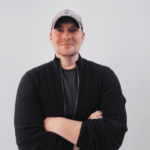 David Scott, former Marine and Black Hawk helicopter pilot turned espionage thriller author, standing with arms crossed and a friendly smile. He is wearing a slightly tipped Maple Leafs hat and a dark gray zippered sweater.